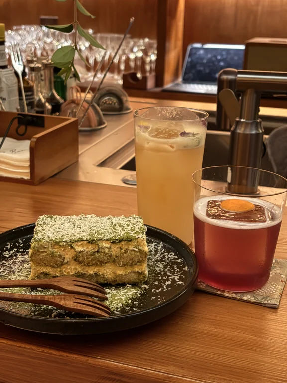 Two cocktails and a slice of cake on the wooden counter at Ashes bar in Dali