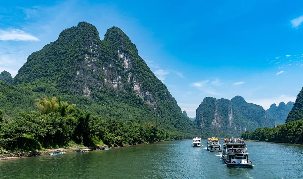 Boats travel between green karst mountains on the Li River near Guilin