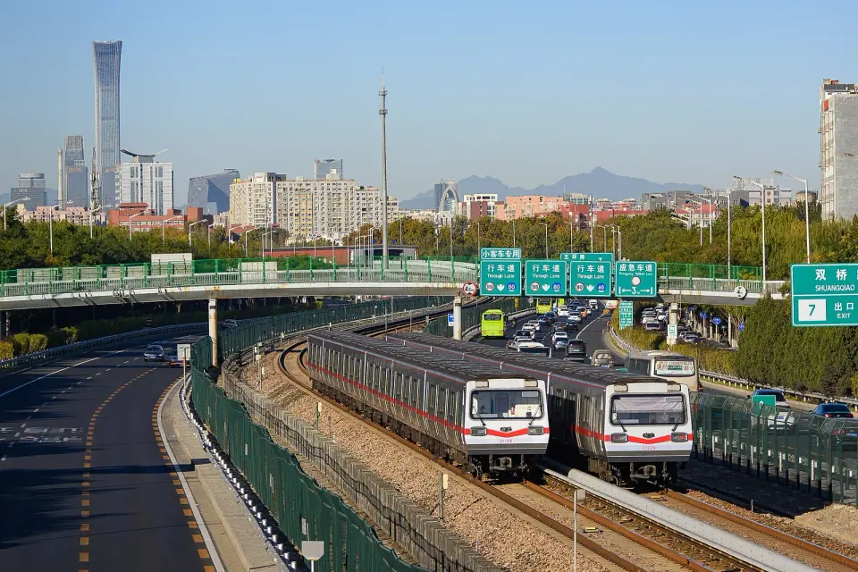 Two Beijing Subway trains on surface tracks with the city skyline behind them