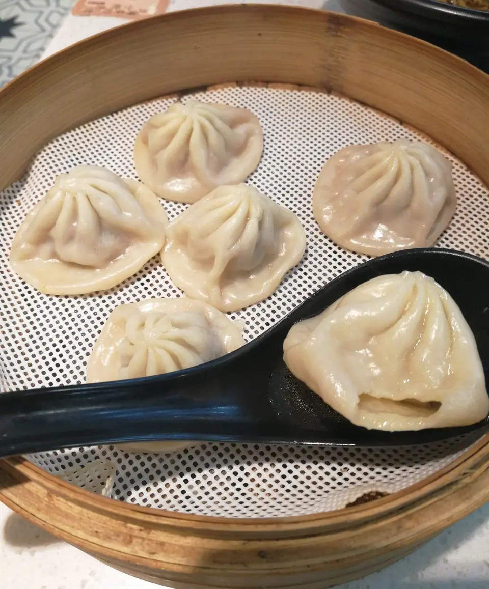 Xiaolongbao soup dumplings in a bamboo steamer with a black serving spoon