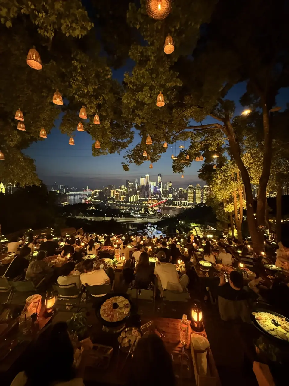 Outdoor tables beneath illuminated trees overlooking Chongqing at Banpo BBQ